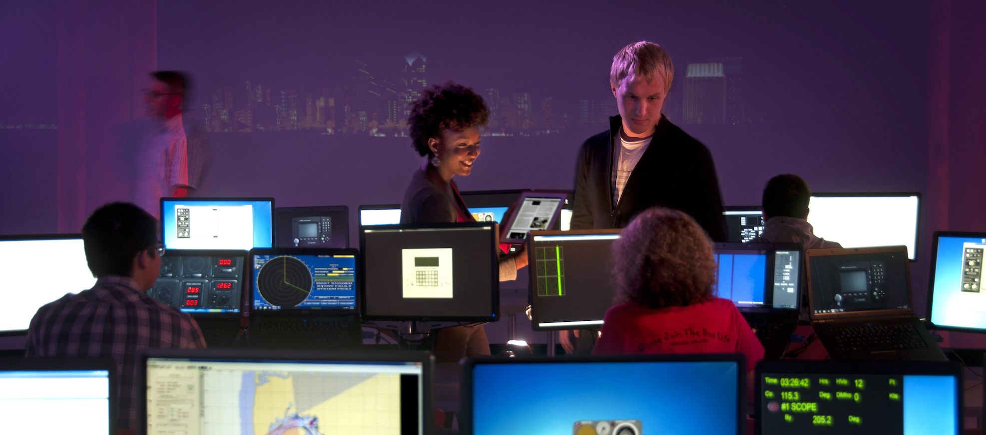 Two people talking in a computer lab surrounded by map graphics