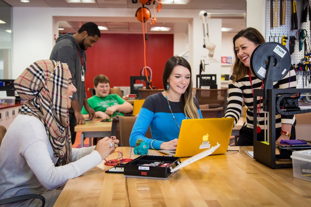 Happy students at a big table with a laptop and electronics kit