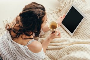 Frau mit Tablet und Kaffee auf Bett